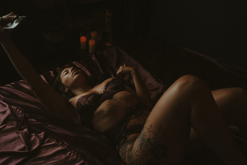 Woman taking her own photo while posing in lingerie during a dark editorial boudoir photography session.